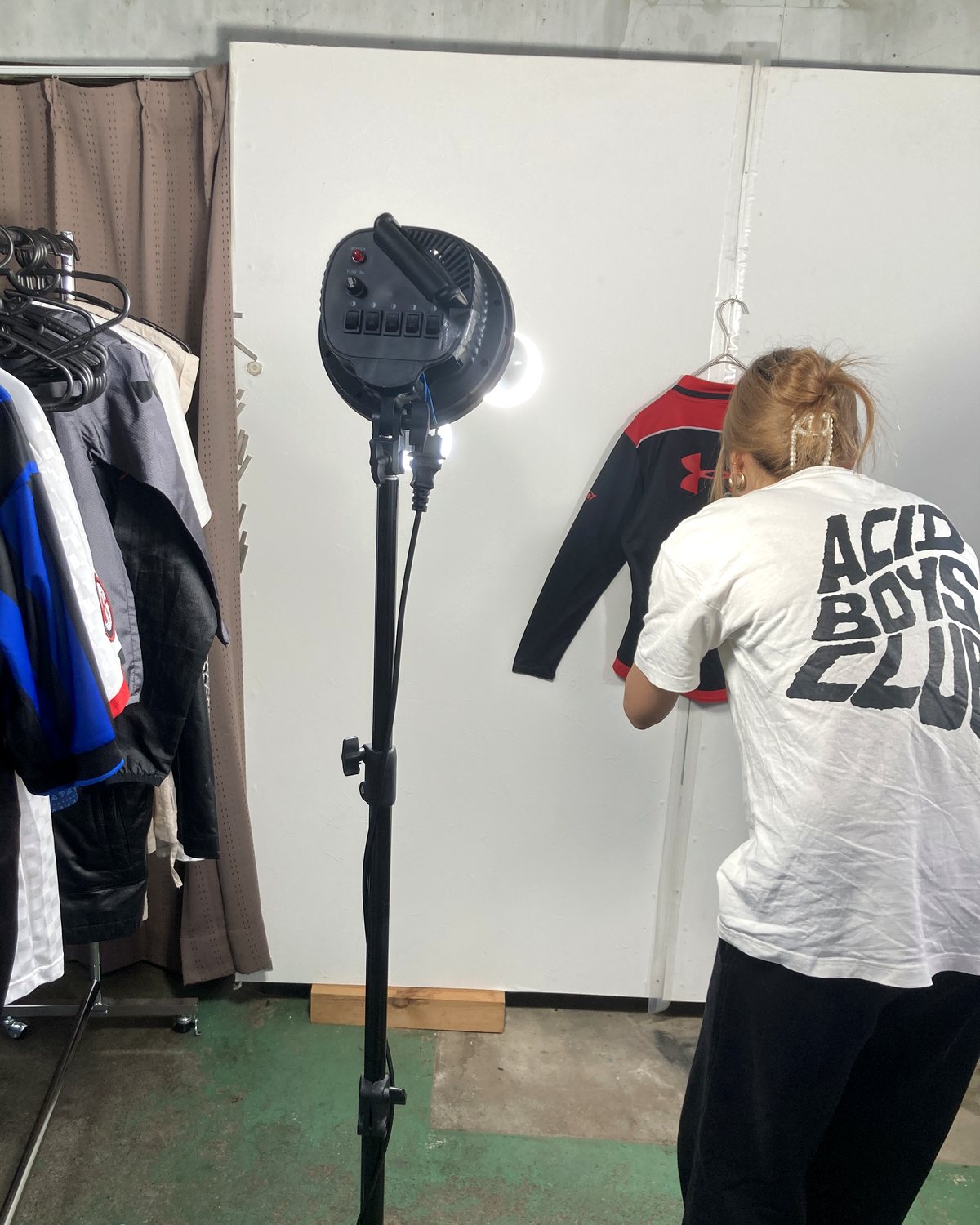 松本市の作業場。白い背景の前でお品物をハンガーに掛け、照明を当てて1点ずつ撮影している様子
